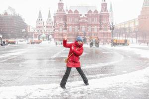 una bella ragazza con una giacca rossa cammina lungo piazza manezhnaya a mosca durante una nevicata e una bufera di neve. gli spazzaneve stanno lavorando in background. foto