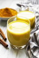 bevanda al latte alla curcuma gialla. latte dorato con cannella, curcuma, zenzero e miele su sfondo di marmo bianco.