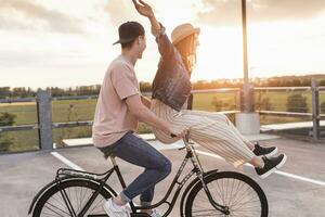 contento giovane coppia insieme su un' bicicletta su parcheggio ponte a tramonto foto