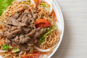 Insalata piccante di noodle istantanei con carne di maiale su piatto bianco - stile cibo asiatico foto