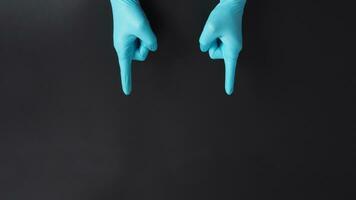 mani indossare blu medico guanti e puntamento dito giù reparti isolato su nero sfondo. foto