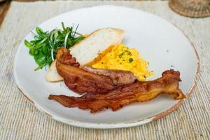 uova strapazzate con pancetta e salsiccia sul piatto per colazione foto