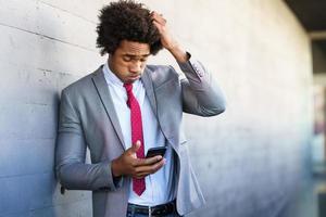 uomo d'affari nero preoccupato usando il suo smartphone all'aperto. foto