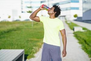 uomo di colore che beve durante l'esercizio. corridore facendo una pausa di idratazione.