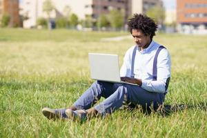 uomo di colore con i capelli afro che usa il suo laptop seduto sullo skateboard foto