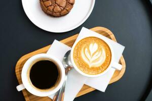 un' tazza di caffè e un' tazza di cappuccino con cioccolato patata fritta biscotti su un' nero tavolo. superiore Visualizza. caffè rompere. foto