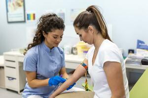 preparazione per sangue test con bella giovane donna di femmina medico medico uniforme su il tavolo nel bianca luminosa camera. infermiera trafigge il del paziente braccio vena con ago vuoto tubo. foto