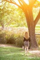 donna lei passeggiate su erba solo intestazione in direzione grande alberi su bordo di prato per fuga sole e calore durante estate. giovane donna a piedi e riposo su erba solo.copia spazio per testo foto