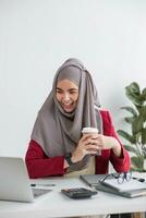 ritratto di bellissimo musulmano donna d'affari sorridente a il telecamera, seduta a sua scrivania. foto