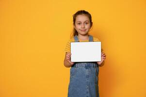 adorabile bambino ragazza mostrando digitale tavoletta con bianca vuoto vuoto schermo, sorridente guardare a telecamera, isolato sfondo foto