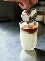 avvicinamento di del barista mano scrosciante caffè in un' bicchiere con frustato latte con ghiaccio mentre preparazione un ghiaccio latte macchiato caffè foto