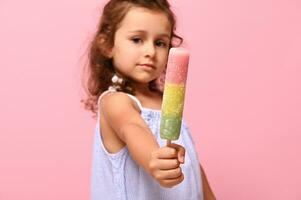 messa a fuoco su Multi colorato colorato congelato succo, ghiaccio crema su bastone nel mani di adorabile ragazza, su di messa a fuoco, isolato su rosa sfondo con copia spazio foto