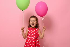 compleanno ragazza vestito nel rosa vestito Tenere colorato palloncini nel sua mani, sorridente guardare a il fotocamera,esprimendo felicità, isolato su rosa sfondo con copia spazio. contento infanzia concetti foto