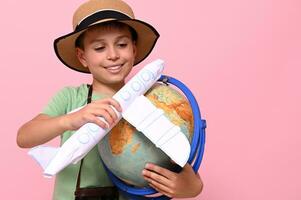 carino ragazzo nel estate cappello detiene un aereo e un' globo nel il suo mani e simula il volo in giro il mondo. turismo, viaggio e aviazione concetti foto