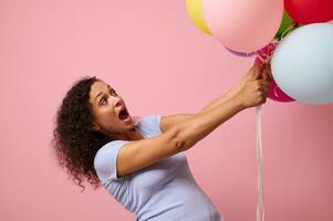 studio tiro per pubblicità di un' sorpreso donna raggiungendo per colorato aria palloncini, in piedi contro rosa sfondo con copia spazio. il concetto di celebrazione, vacanze, anniversario e i regali. foto