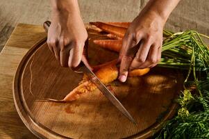 superiore Visualizza di femmina mani taglio, tritare, affettare fresco crudo bambino carota su un' di legno tavola. avvicinamento di mano con coltello taglio fresco verdura. foto