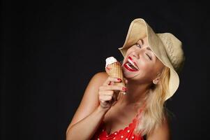 attraente caucasico bionda donna nel estate cappello Tenere un' delizioso gelato nel sua mani e sorrisi con bellissimo trentadue denti Sorridi guardare a telecamera, isolato al di sopra di nero sfondo con copia anno Domini spazio foto