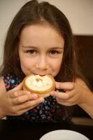 avvicinamento ritratto di un' carino poco bambino ragazza degustazione un' dolce francese al forno dolce - un' Limone tortino, sorrisi guardare a telecamera foto