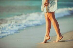 femmina gambe su il spiaggia avvicinamento. donna nel vestito a piedi su il spiaggia foto