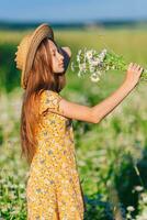 ritratto di ragazza nel un' giallo vestito e cannuccia cappello su un' camomilla campo nel estate foto