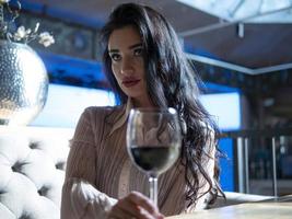 ritratto di una ragazza seduta a tavola con un bicchiere di vino rosso foto
