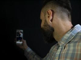uomo con barba e baffi guarda nel telefono e fa un selfie