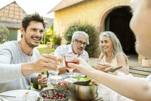 contento famiglia mangiare insieme nel il giardino, tintinnante bicchieri foto