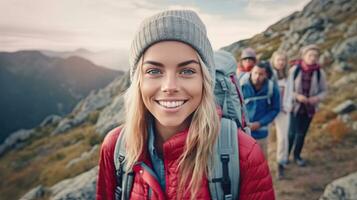 un' sorridente giovane donna escursionista con zaino guardare a telecamera con gruppo di amici escursionisti sorge per il superiore di il collina. escursionista, turista campo. generativo ai foto