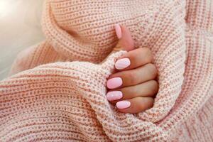 femmina mani con bellissimo di forma ovale chiodo, Opaco rosa manicure avvicinamento su un' rosa a maglia maglione sfondo. Gommalacca. foto
