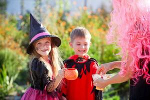 bambini trucco o trattare nel Halloween costume . un' poco ragazzo e un' ragazza nel tute ricevere caramella a partire dal un' donna . foto