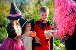 gruppo bambini trucco o trattare nel Halloween costume . un' poco ragazzi e un' ragazza nel tute ricevere caramella a partire dal un' donna . foto