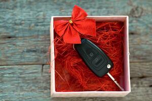 auto chiave nel un' regalo scatola con un' rosso nastro arco su un' di legno sfondo. regalo per Natale o San Valentino è giorno o presente un astratto concetto. foto
