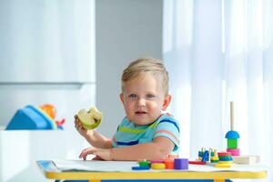 un' poco ragazzo 2 anni mangia un Mela e è giocato con di legno palle. educativo logica giocattoli per bambini. Montessori Giochi per bambino sviluppo. foto