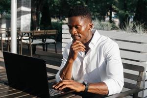 uomo d'affari afroamericano, lavora al computer portatile in un bar, libero professionista foto