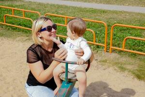 mamma rotoli bambino figlia su un' swing su il terreno di gioco, parlando con il bambino foto