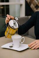 un' donna versa mare spinoso tè a partire dal un' teiera in un' boccale foto