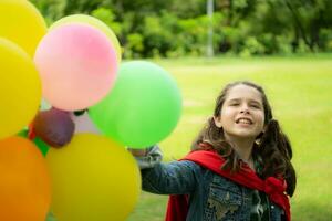 su un' bellissimo giorno nel il parco, un' giovane ragazza gode sua vacanza. giocoso con un' rosso supereroe costume e maschera. foto