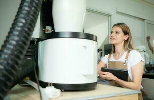 giovane donna nel grembiule utilizzando digitale tavoletta per controllo qualità di di caffè fagioli con digitale roaster foto