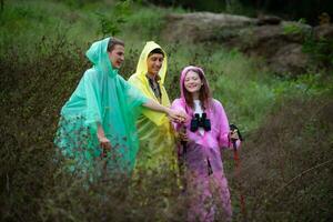 gruppo di amici nel impermeabili con zaini su un' escursione nel il foresta, preparare per escursioni a piedi dopo il pioggia ha fermato. foto