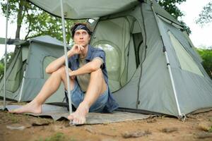 giovane uomo seduta nel davanti di tenda a campeggio nel il campagna foto