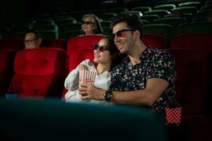 nel un' cinema, un' giovane coppia paio indossare 3d bicchieri orologi film e mangia Popcorn. foto