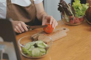 delizioso frutta e verdure su un' tavolo e donna cucinando. casalinga è taglio verde cetrioli su un' di legno tavola per fabbricazione fresco insalata nel il cucina. foto