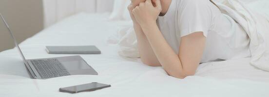 efficiente giovane del Millennio ragazza seduta su un' letto nel il mattina, usi il computer portatile computer e mangia Cornetti e bevande caffè per prima colazione foto