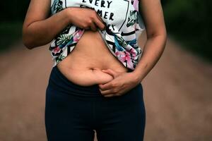 donne corpo Grasso gonfiarsi. obeso donna mano Tenere eccessivo pancia Grasso. dieta stile di vita concetto per ridurre pancia e forma su salutare stomaco muscolo. foto