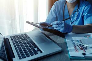 medico Lavorando su il computer portatile computer, scrittura prescrizione appunti con disco informazione carta cartelle su scrivania nel ospedale o clinica, assistenza sanitaria e medico concetto. messa a fuoco su stetoscopio foto