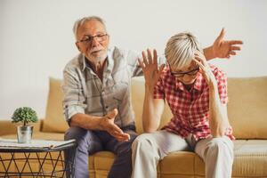 anziano coppia seduta nel vivente camera e discutere. donna è arrabbiato mentre uomo è scusarsi. foto