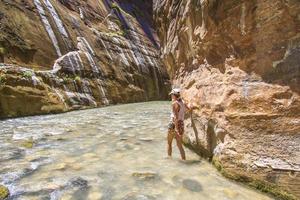 donna che cammina attraverso un fiume in fondo a un canyon foto