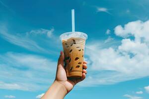 mano Tenere ghiacciato caffè nel un' plastica tazza con un' blu cielo e nube sfondo. ai generato foto