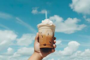 mano Tenere ghiacciato caffè nel un' plastica tazza con un' blu cielo e nube sfondo. ai generato foto