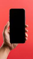 mano Tenere smartphone con un' nero vuoto schermo isolato su un' rosso sfondo. ai generato foto